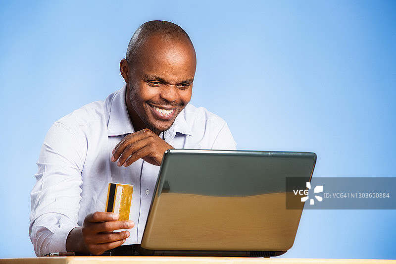 电商购物或网上银行：英俊的男人在笔记本电脑旁拿着信用卡图片素材