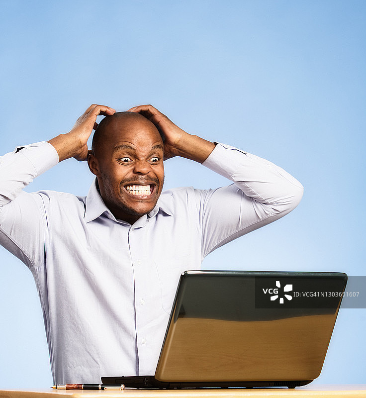 在笔记本电脑前沮丧绝望地抱头的英俊男人图片素材