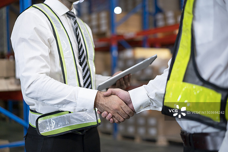 两位头戴安全帽的男商人在仓库中握手，合作愉快图片素材