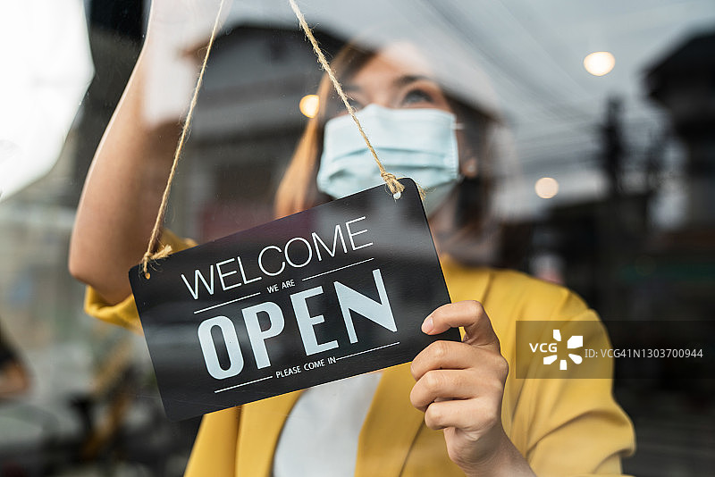 疫情后重新开业的咖啡店，佩戴口罩的女店主在门口欢迎顾客，支持本地商家图片素材