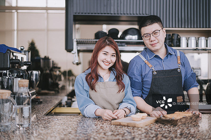 在咖啡馆吧台看着镜头的亚洲小企业主夫妇图片素材