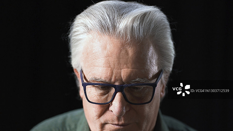 年长的男人戴着眼镜向下看图片素材