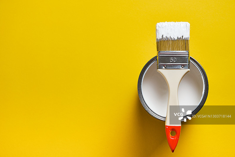 白色油漆罐上的刷子，明亮的黄色背景。绘画和维修工作。创造力、建筑工作、爱好概念图片素材