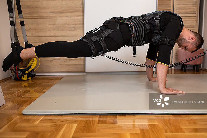 健壮的年轻男人穿着EMS训练服做悬挂平板支撑图片素材