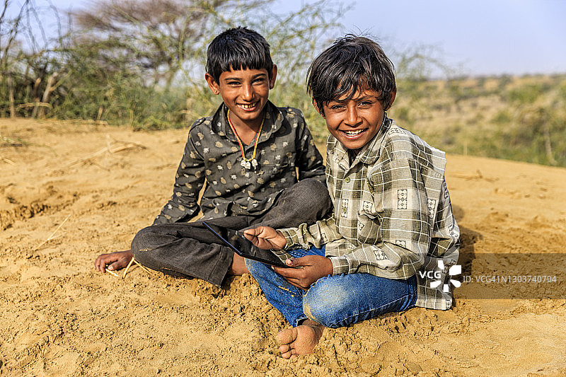 快乐的印度男孩在印度沙漠村庄使用平板电脑图片素材