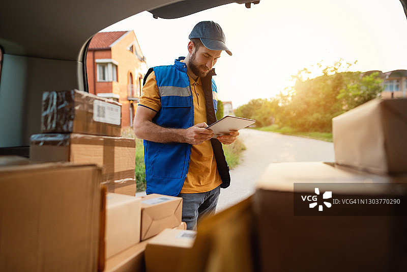 年轻的快递员站在后备箱前查看平板电脑图片素材