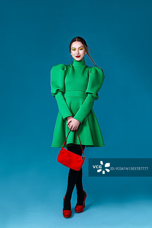 穿着绿色连衣裙，手提红色手提包的漂亮女人图片素材