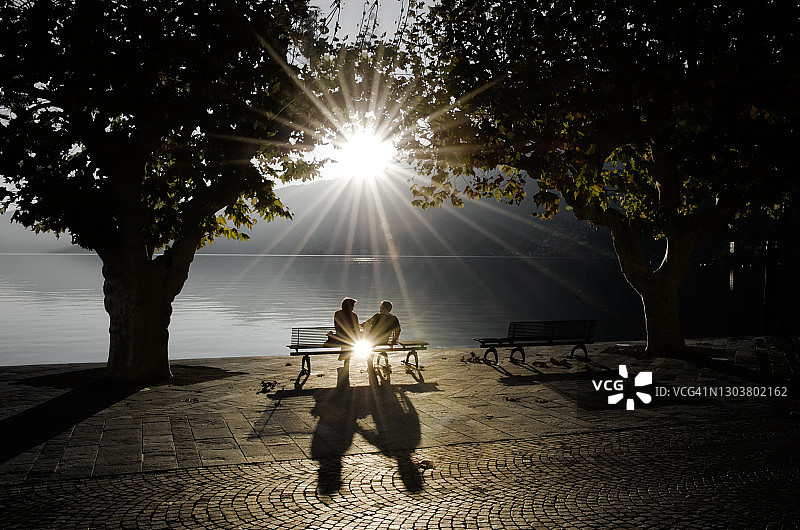 情侣坐在海滨长椅上欣赏高山湖泊的阳光图片素材