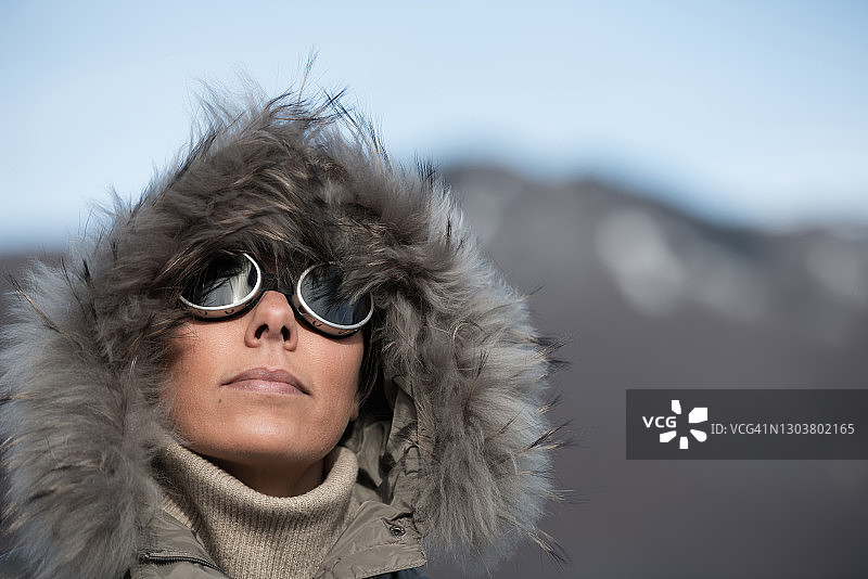 戴滑雪镜、穿冬季连帽外套的女人在阳光明媚的山中图片素材