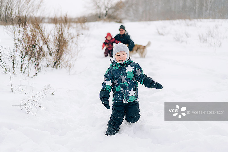 小男孩在雪地里玩耍，一个男人带着孩子和狗坐在男孩身后图片素材