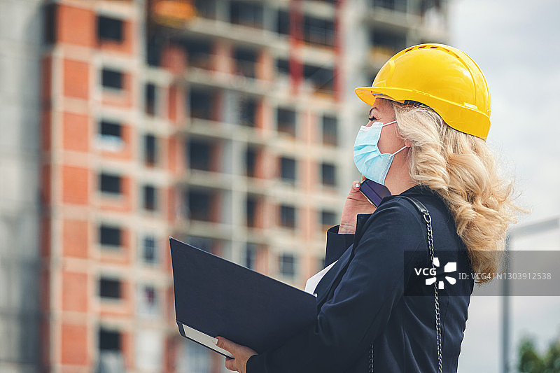 新冠疫情期间，在建筑工地检查工作时使用手机的女施工经理图片素材