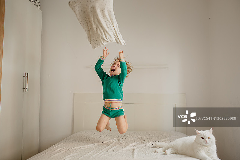 男孩在床上跳跃，猫咪在旁边图片素材