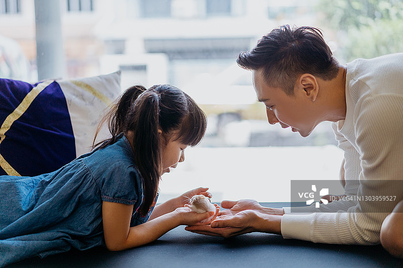 年轻的亚洲女孩在家和父亲一起玩宠物仓鼠图片素材