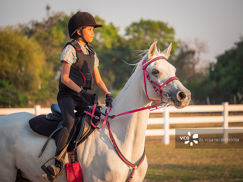 在农场享受骑马乐趣的年轻亚洲女孩，在泰国骑着白色阿拉伯马进行骑术训练图片素材