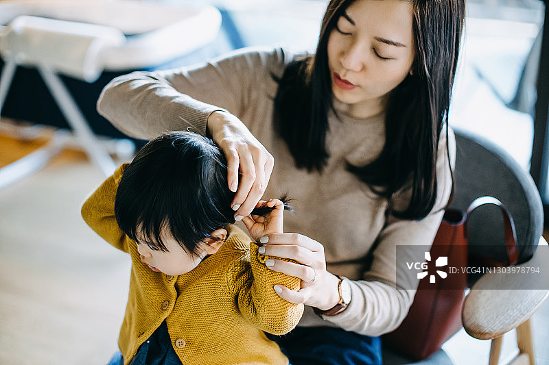 年轻的亚洲妈妈在出门前为小女儿扎头发并在家穿好衣服，家庭生活方式图片素材