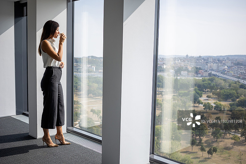美丽的职业女性在咖啡休息时间站在大办公室的窗边图片素材