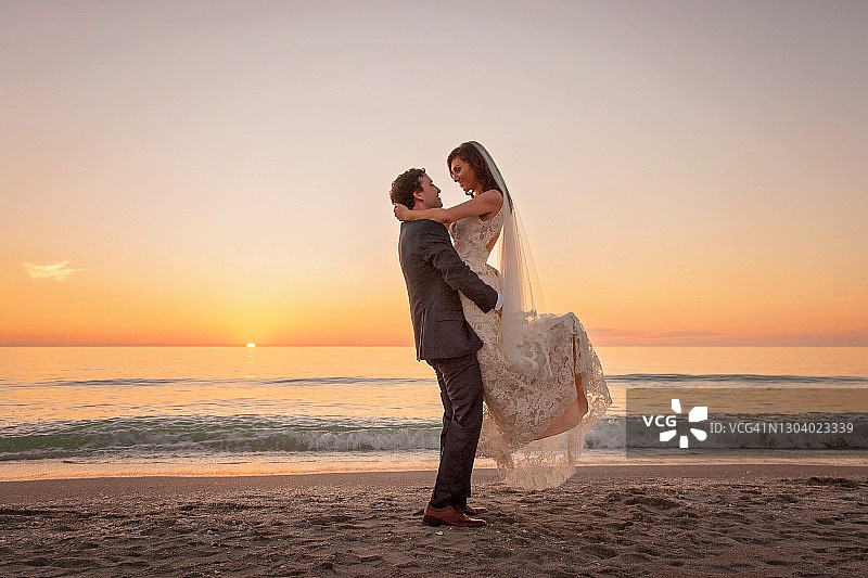 夕阳与大海背景下的新郎托举新娘剪影图片素材