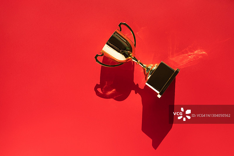 鲜红色背景上带有阴影的金属金色高脚杯俯视图。目标成就概念。年度流行色图片素材