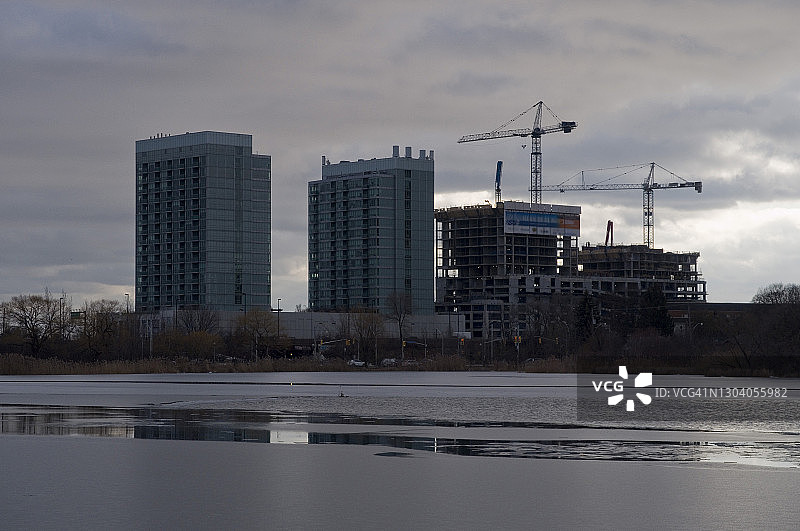 冰冷的池塘旁住宅楼施工现场的吊车图片素材