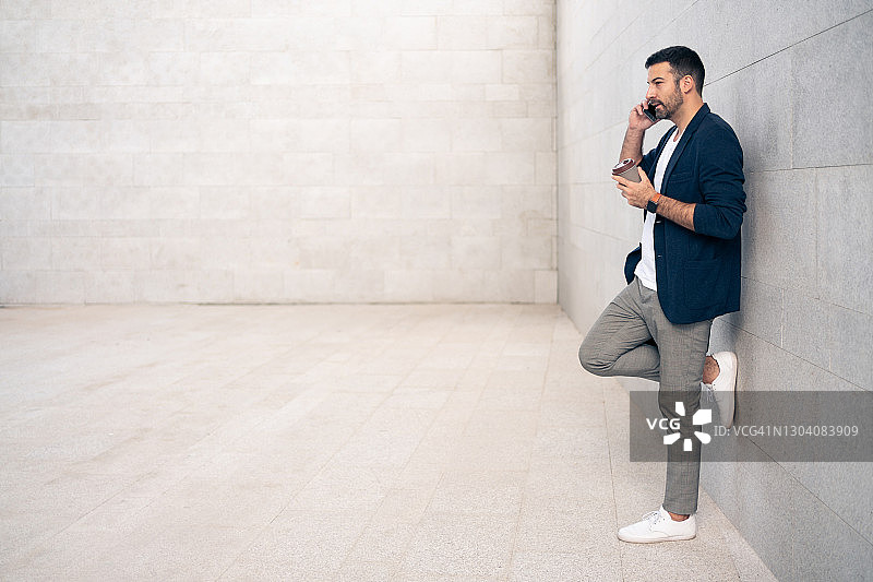 年轻男子靠墙打电话的侧面照图片素材
