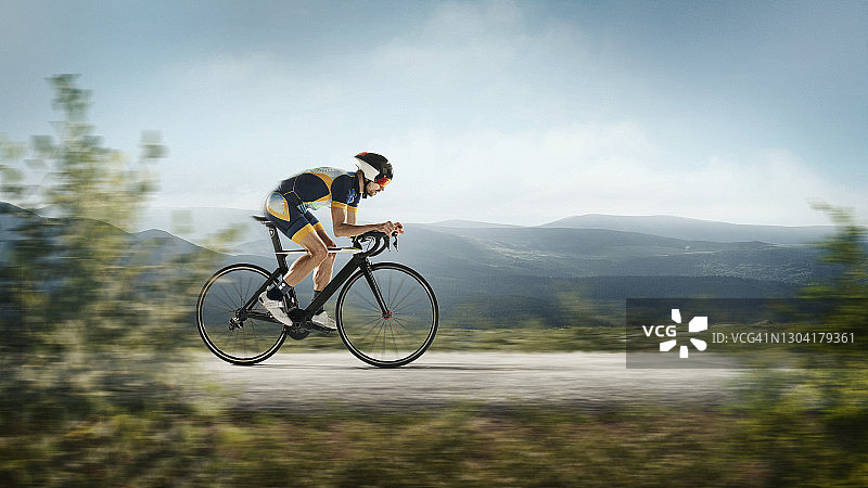 在山地背景下训练的铁人三项男运动员。 一名白人铁人三项运动员正在练习自行车，身穿运动装备图片素材
