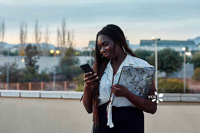 在校园里看手机的黑皮肤年轻学生图片素材