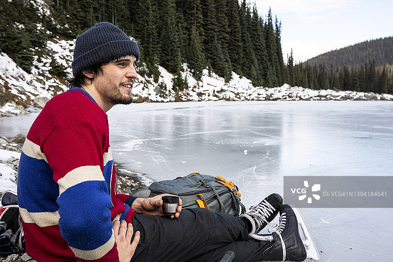 在冰冻的湖边休息并饮用热饮的年轻曲棍球运动员图片素材