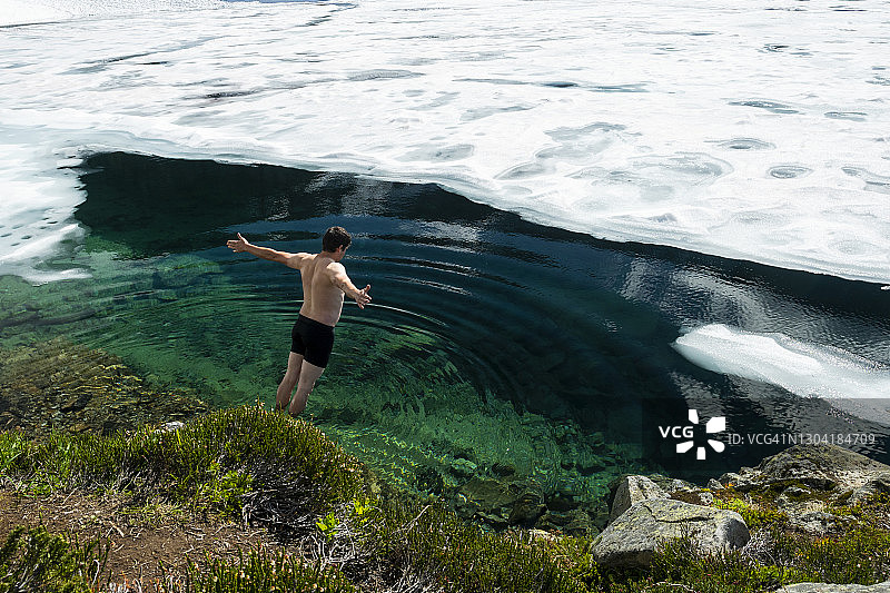 在阳光明媚的日子里，一名赤膊男子张开双臂掉入冰冻湖的冷水中的背影图片素材
