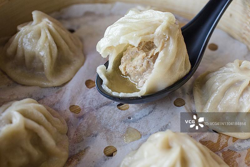 蒸汽笼屉里勺子上半个汤包的特写图片素材