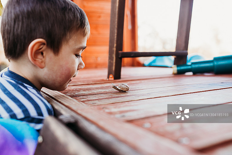 小男孩研究蜗牛在操场上爬行的特写图片素材