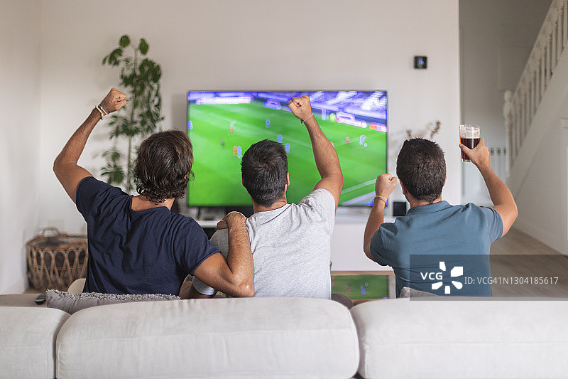 三个朋友在家看足球比赛喝啤酒图片素材