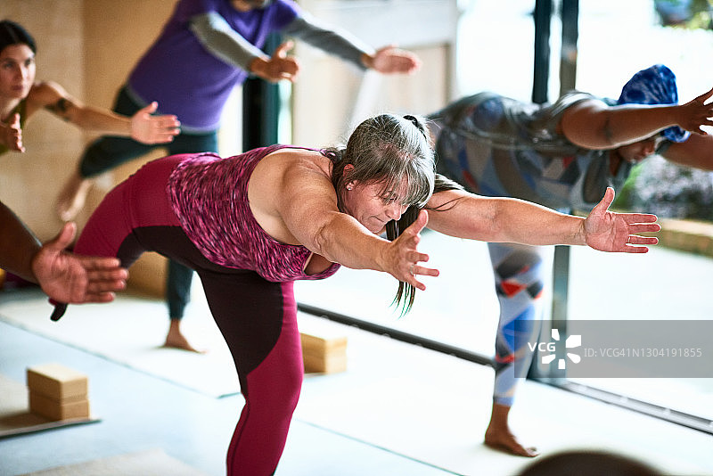 在瑜伽课上做战士第三式的中年妇女图片素材