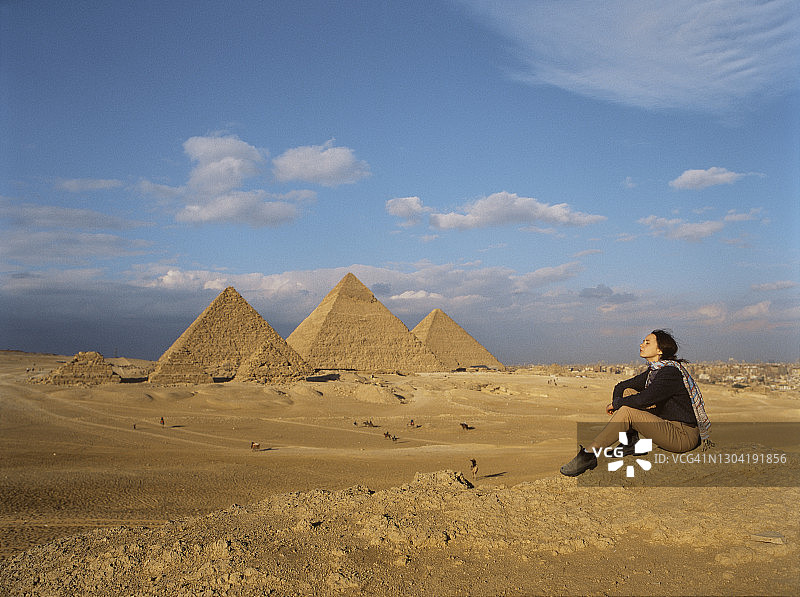 坐在吉萨金字塔附近沙漠中的女人图片素材