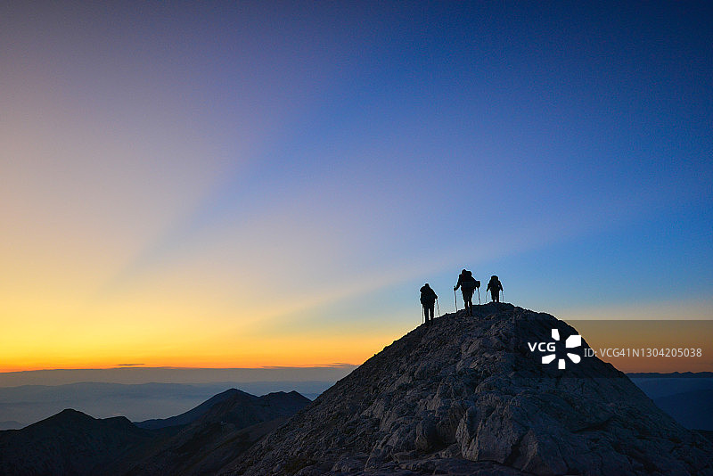 日落时山顶上三个徒步旅行者剪影图片素材