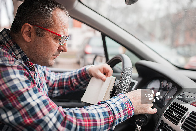 戴眼镜的男人检查他的汽车，坐在驾驶座上写东西图片素材