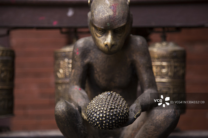 尼泊尔加德满都金庙庭院中手捧菠萝蜜的黄铜猴子图片素材