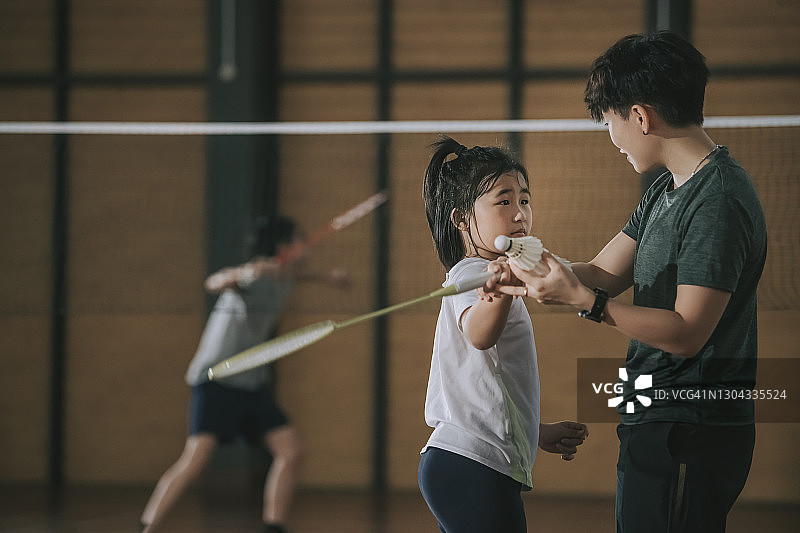 中国亚洲女教练在羽毛球场指导她的学生练习姿势图片素材