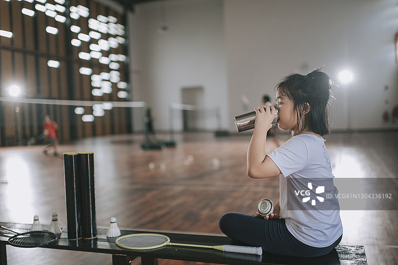 亚洲华裔羽毛球年轻女孩运动员在场边喝水休息图片素材