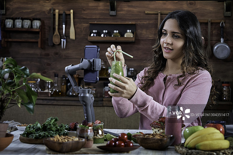 在乡村厨房里录制健康冰沙食谱视频博客的年轻西班牙裔女子图片素材