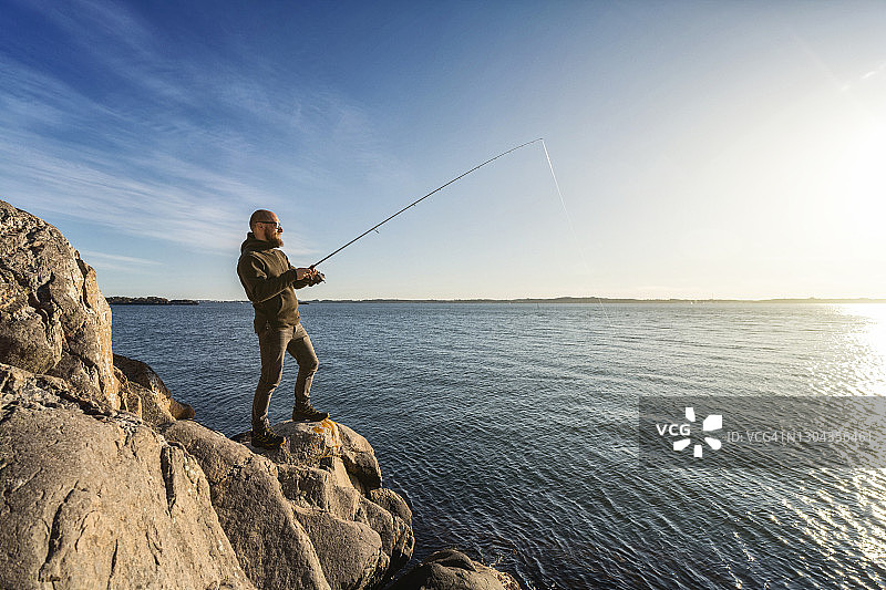 男人在海边的岩石上用钓竿钓鱼图片素材
