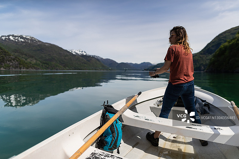 在挪威峡湾，女子在小船上用鱼竿钓鱼图片素材