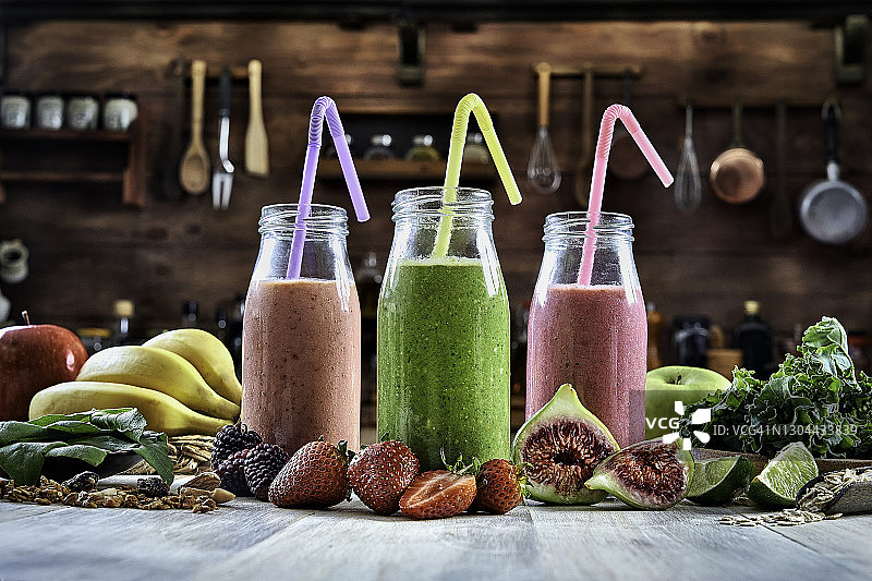 健康食品：乡村风桌子上放着三瓶香蕉黑莓、草莓和绿色排毒思慕雪，配有吸管图片素材