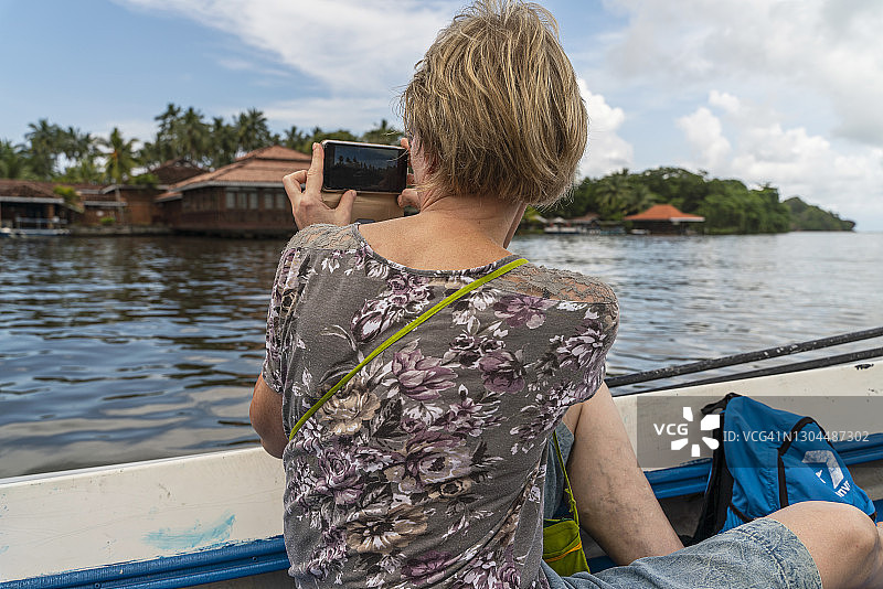年长的白人短发妇女在斯里兰卡本托塔河乘船游览时用智能手机拍照图片素材