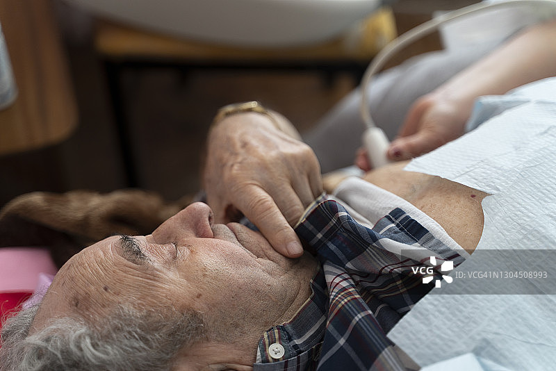 医疗技术员护士在家中使用便携式超声设备为97岁高龄男性患者进行心脏超声检查图片素材