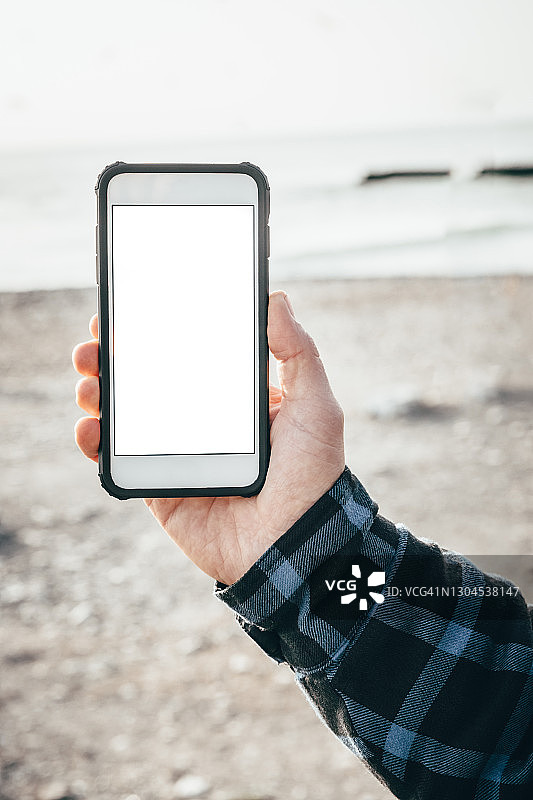 海滩背景中男性手持白色屏幕智能手机样机图片素材
