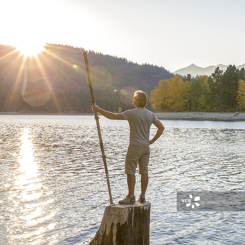 男人拄着拐杖站在湖边的树桩上，日出图片素材