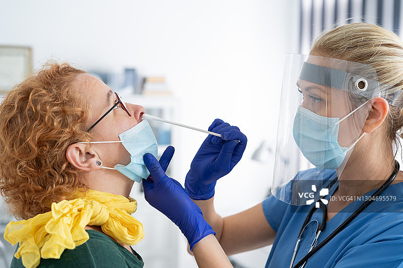 戴防护面罩的医生为一名妇女进行鼻拭子取样，以检测可能的新冠病毒感染图片素材