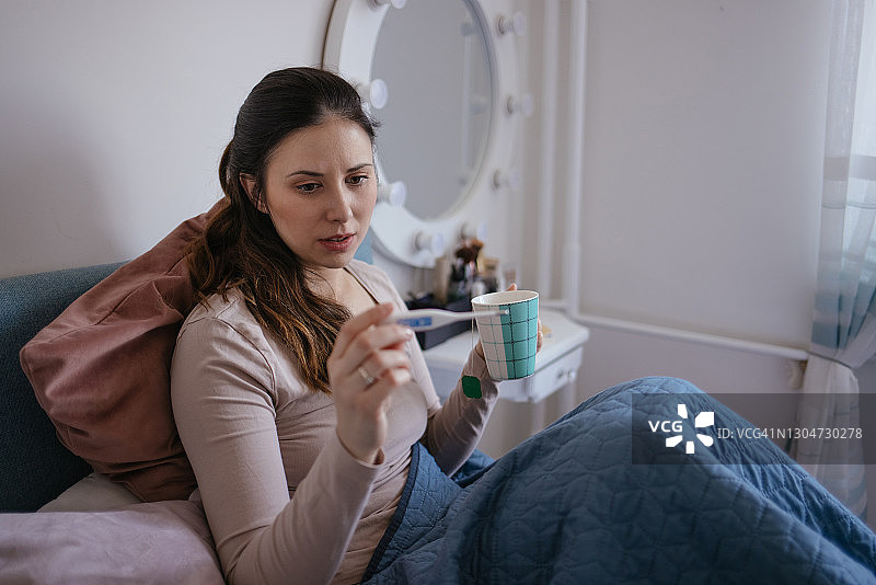 生病的女人在床上用电子体温计测量体温图片素材