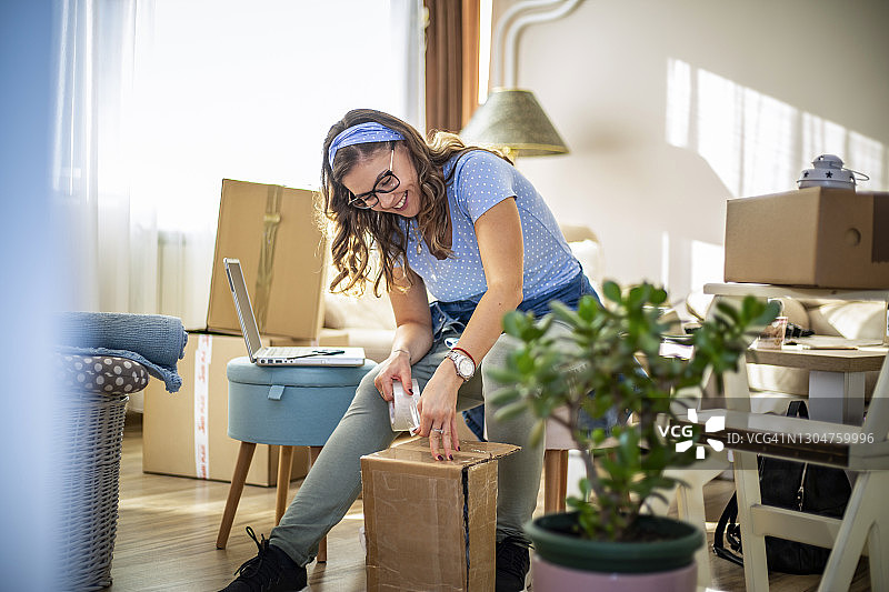 年轻女子搬家。梦想成真！一位年轻漂亮的女子正在思考如何在新家打开所有物品，新的开始！图片素材