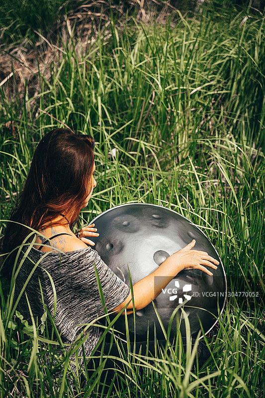 长发女人坐在高高的草丛中演奏手碟图片素材